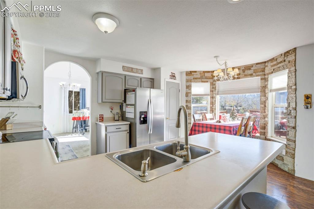Image 14 of 27: Kitchen with a chandelier, gray cabinetry, and plenty of natural light