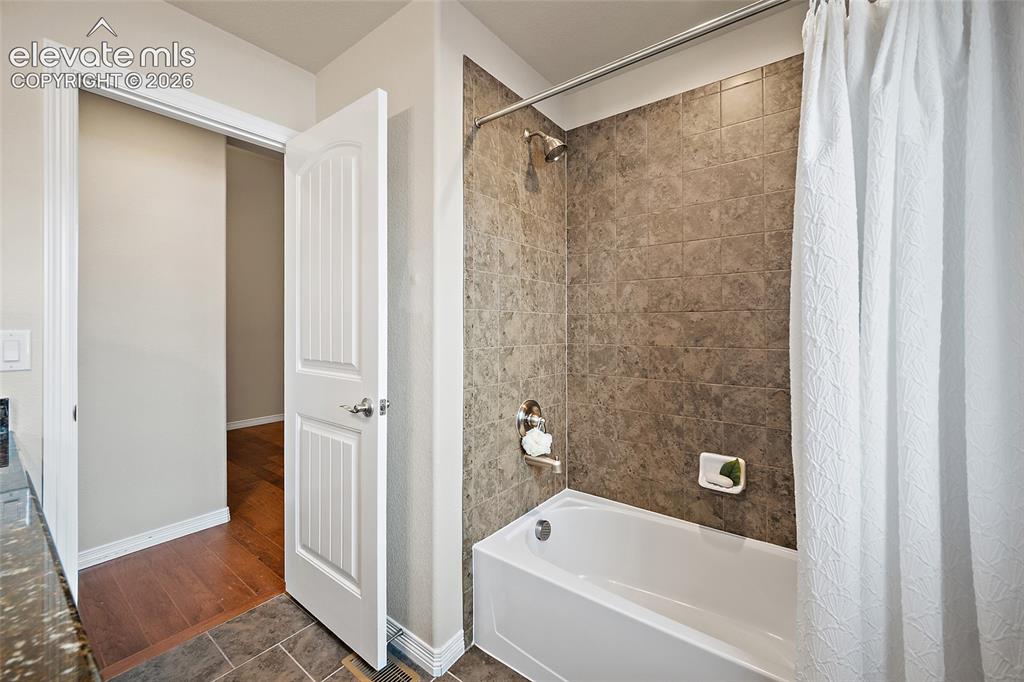 Image 16 of 29: Bathtub with tiled shower surround and chrome fixtures