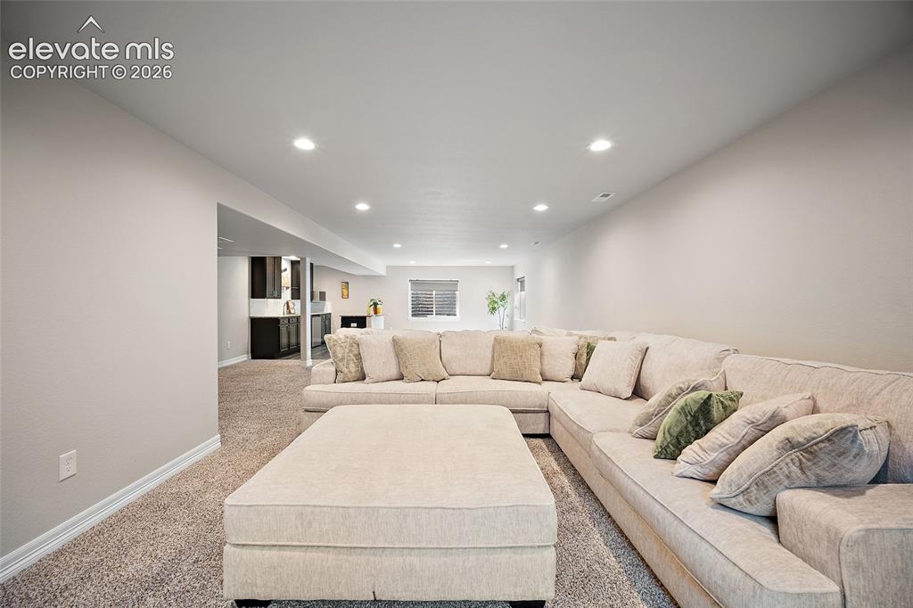 Image 17 of 29: Recessed ceiling lighting illuminates the carpeted living area with light-t