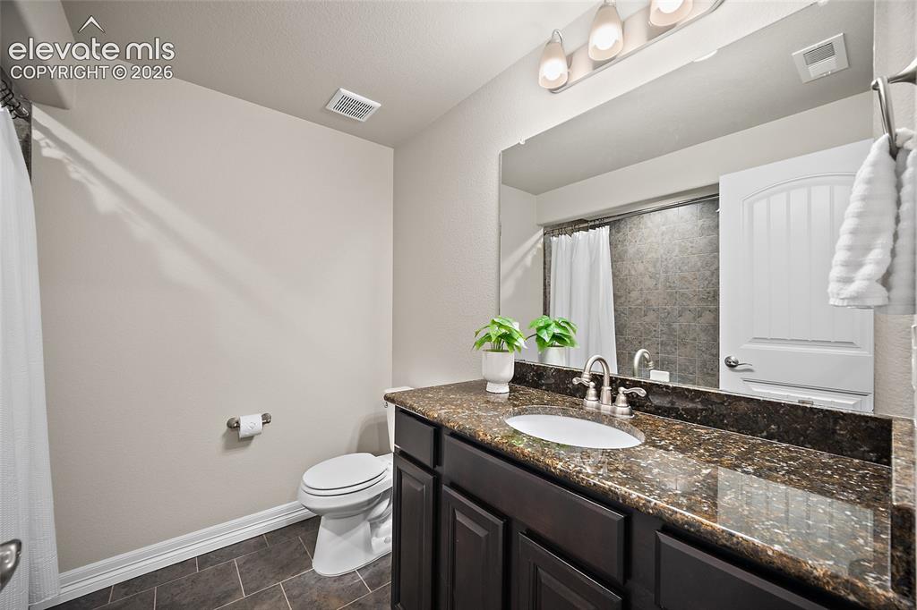 Image 24 of 29: Vanity with a dark stone countertop, a drop-in sink, and a chrome faucet