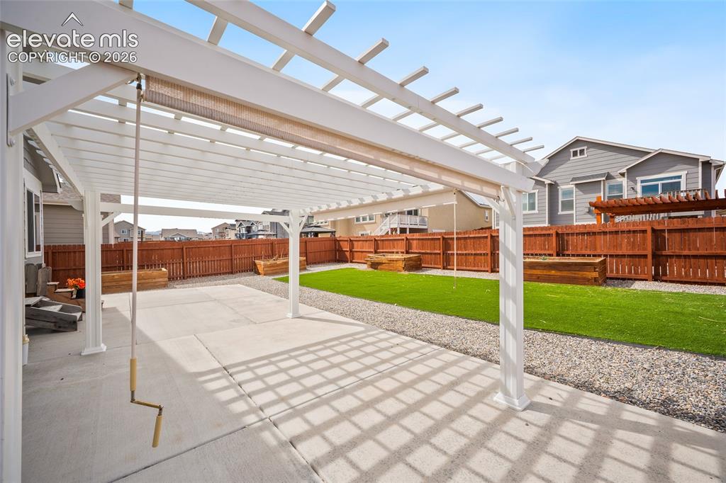 Image 26 of 29: Spacious patio featuring a white pergola with a retractable shade, artifici