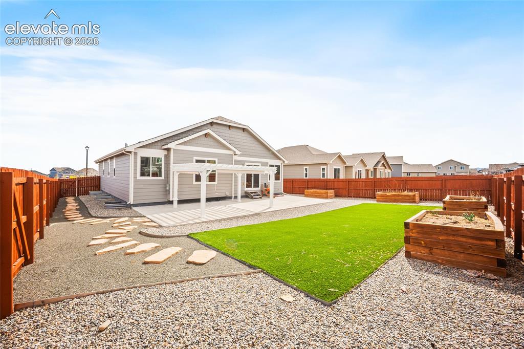 Image 27 of 29: Expansive backyard featuring a gray siding exterior, pergola-covered patio,