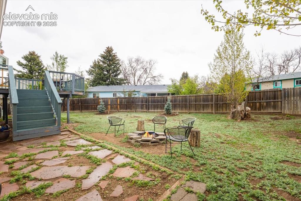 Image 49 of 50: Expansive fenced backyard featuring a composite deck with stairs, a flagsto
