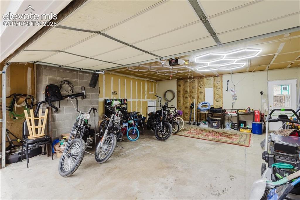 Image 6 of 50: Spacious garage with concrete flooring, exposed insulation, a privacy door,