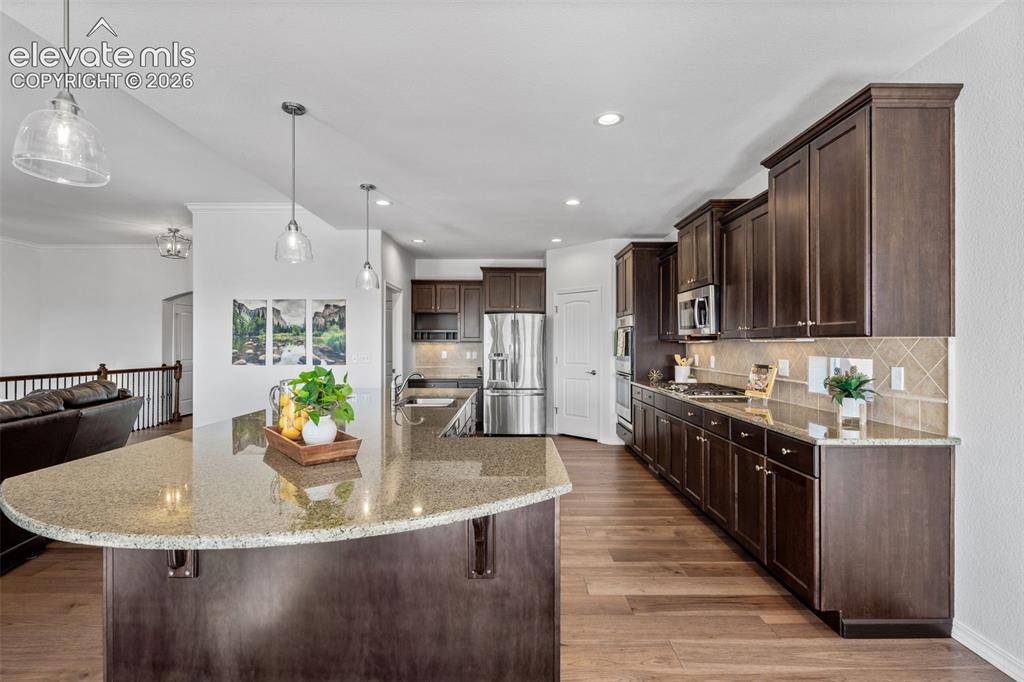 Image 16 of 50: Kitchen island featuring a curved granite countertop and pendant lighting