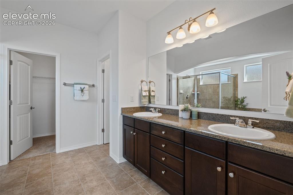 Image 30 of 50: Spacious bathroom featuring a double vanity with stone countertops, dark wo