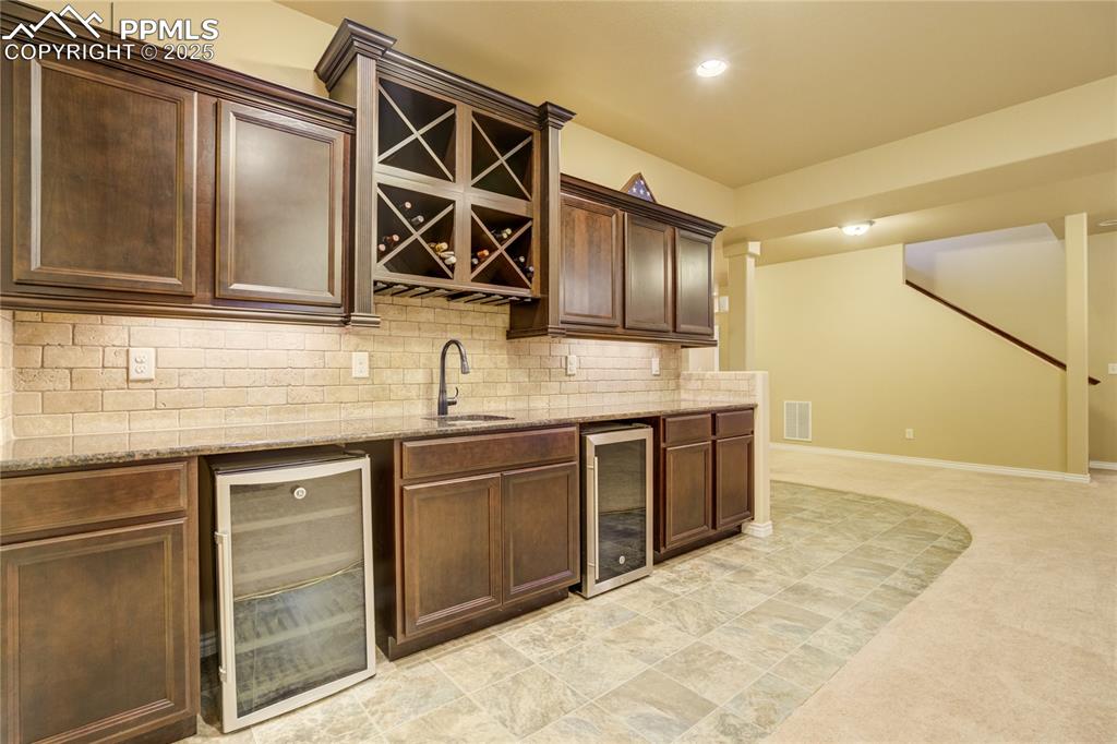 Image 34 of 50: Thoughtfully designed wet bar with granite, tile backsplash, built-in wine 
