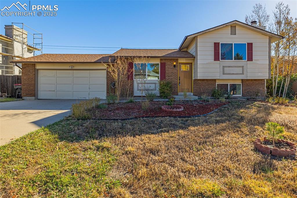 Image 3 of 33: Split level home with driveway, brick siding, a garage, and a front lawn