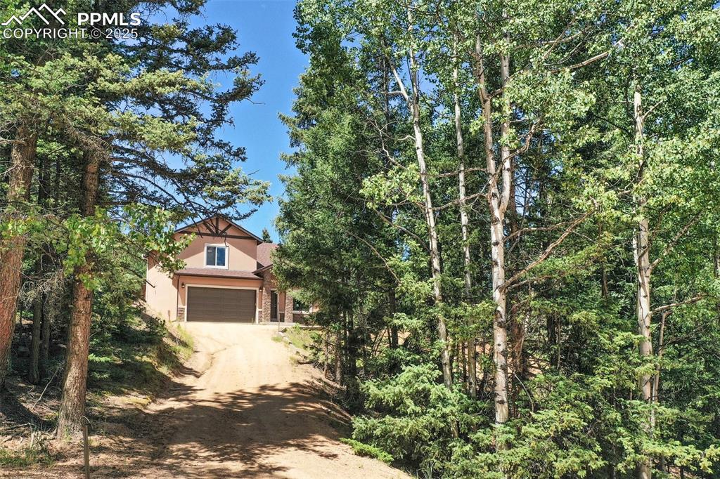 Image 2 of 46: View of front of house featuring dirt driveway, stucco siding, and a garage