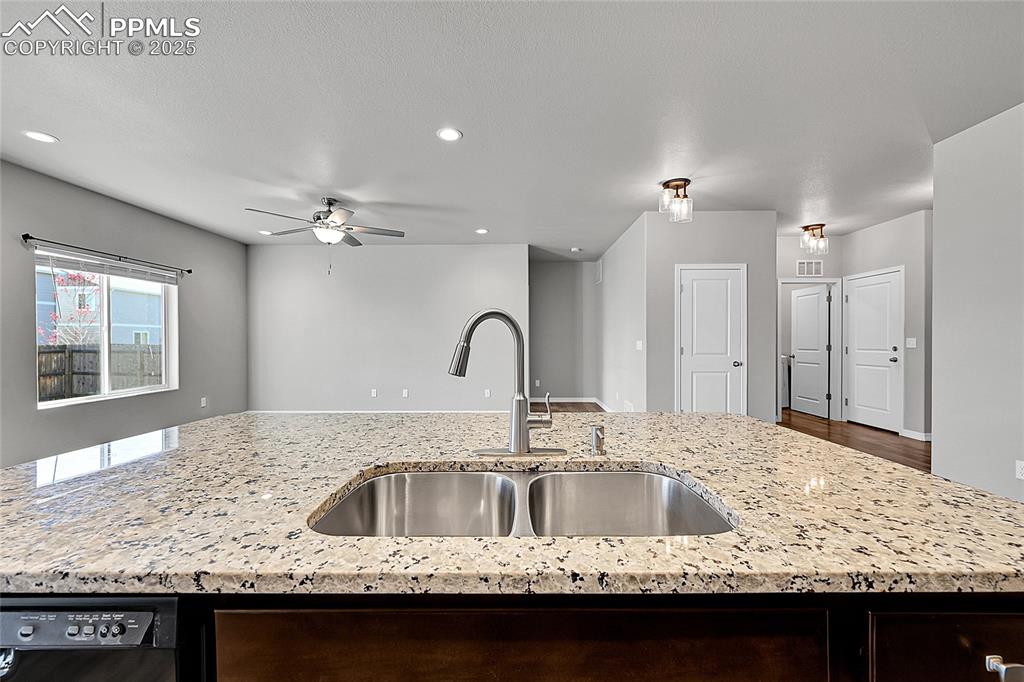 Image 10 of 43: Kitchen with light stone countertops, black dishwasher, recessed lighting,