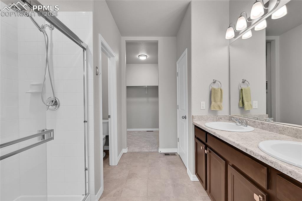 Image 16 of 43: Primary bathroom featuring double vanity, a walk in closet, a shower stall,