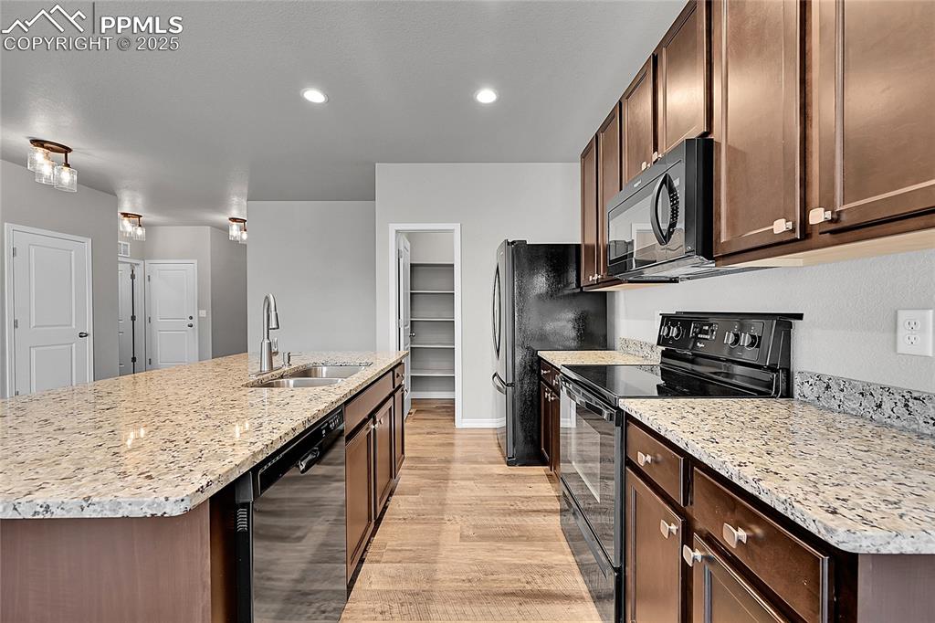 Image 9 of 43: Kitchen with black appliances, dark brown cabinets, light stone counters, a