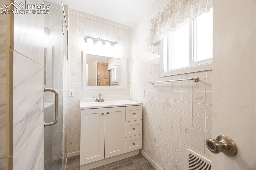 Image 14 of 34: Bathroom with tile walls, a shower stall, vanity, and wood finished floors