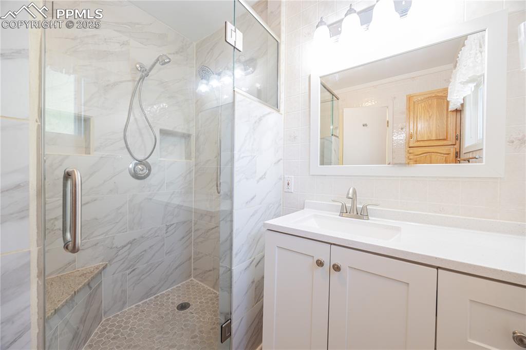Image 15 of 34: Bathroom featuring tile walls, a stall shower, vanity, and backsplash