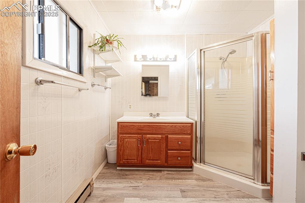 Image 16 of 34: Bathroom featuring baseboard heating, vanity, tile walls, a stall shower, a