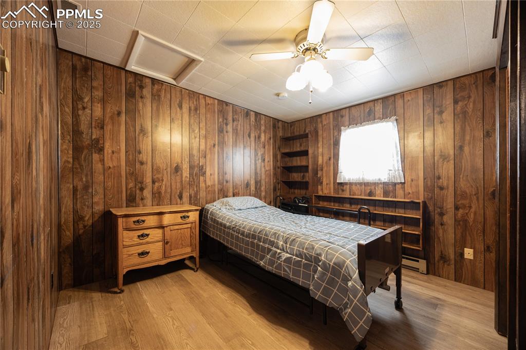 Image 17 of 34: Bedroom with wooden walls, light wood-style flooring, a baseboard radiator,