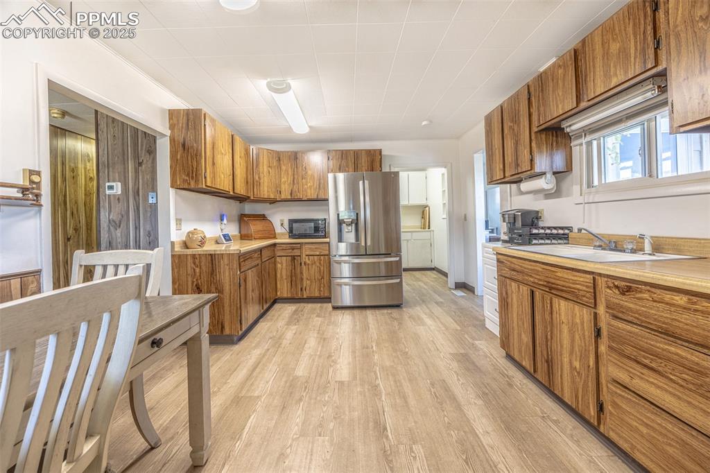 Image 7 of 34: Kitchen with brown cabinets, stainless steel fridge with ice dispenser, lig
