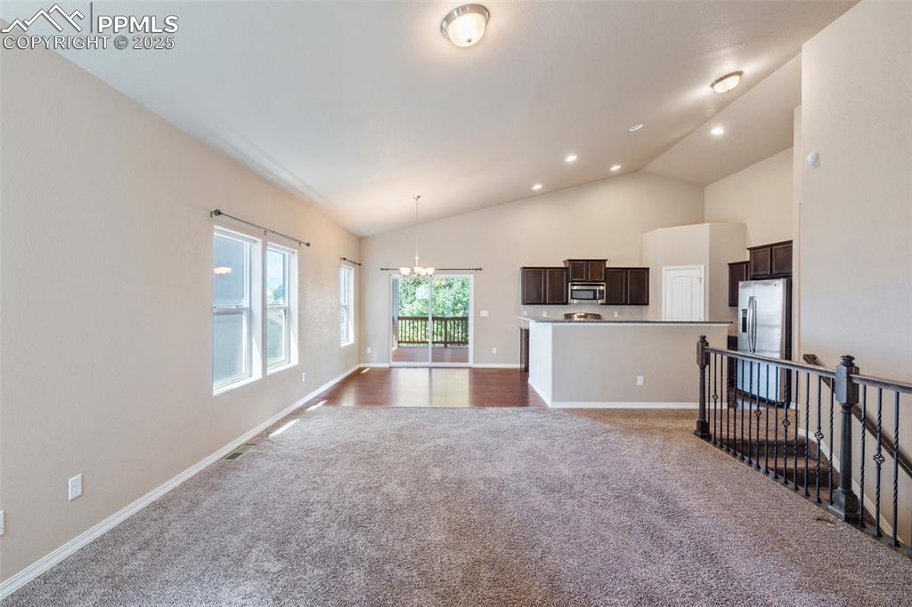 Image 5 of 45: Unfurnished living room with dark carpet, a chandelier, high vaulted ceilin