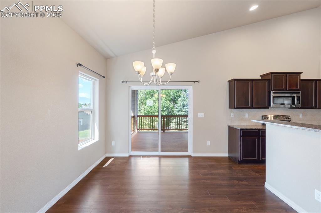 Image 9 of 45: Kitchen with dark brown cabinets, lofted ceiling, a chandelier, light stone