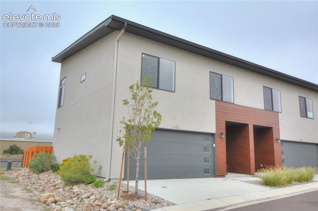 Caption: Modern stucco exterior with flat roofline, integrated garage, wood-finish facade elements, and conte