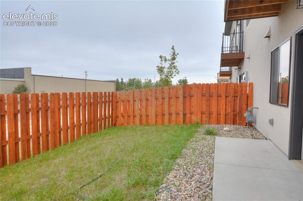 Image 21 of 25: Private outdoor space featuring a wood fence, a patch of grass, and a concr