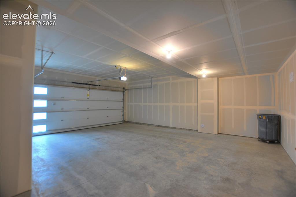 Image 23 of 25: Spacious garage with an overhead door featuring frosted window panels, conc