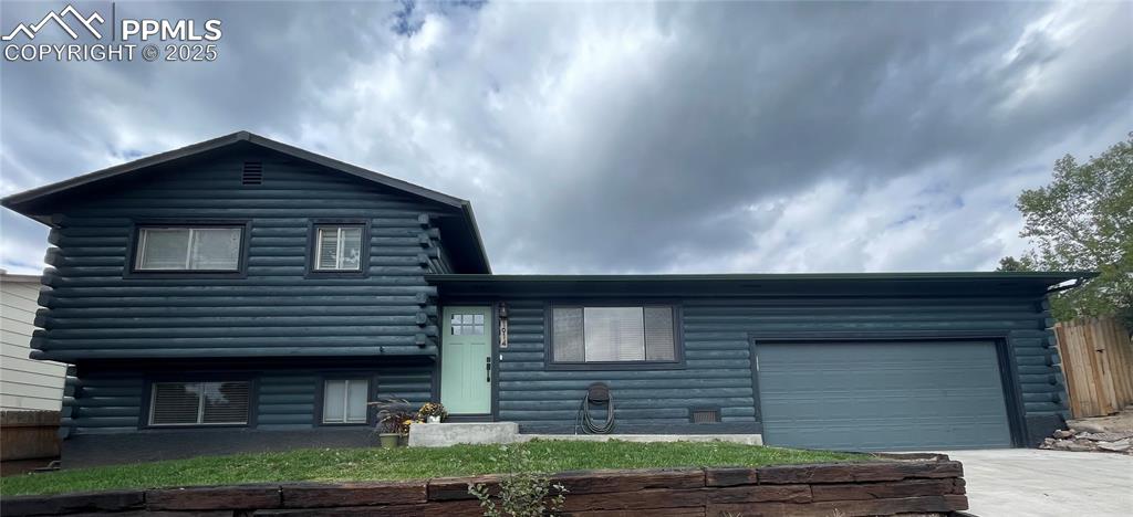 Caption: View of front of property with an attached garage, driveway, and log exterior
