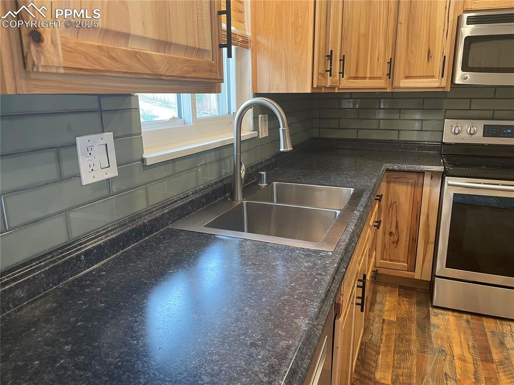 Image 13 of 39: Kitchen featuring brown cabinetry, decorative backsplash, and dark wood fi