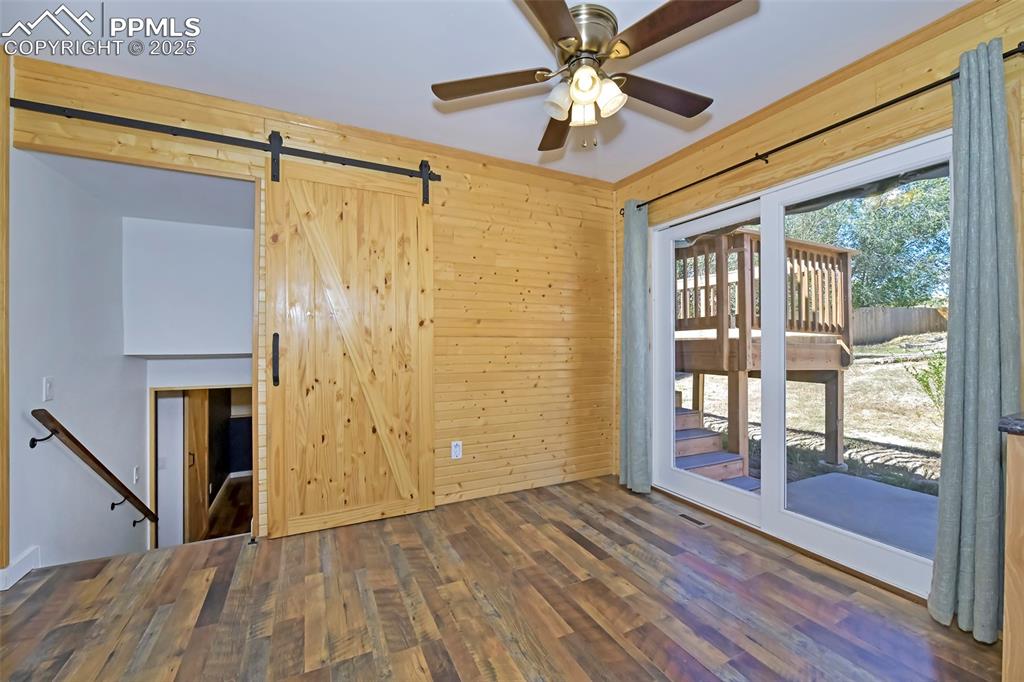 Image 14 of 39: Unfurnished room featuring a barn door, wood walls, wood finished floors, a