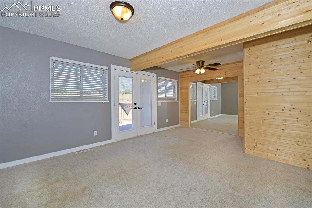 Image 16 of 39: Carpeted spare room with french doors, wooden walls, a textured ceiling, be