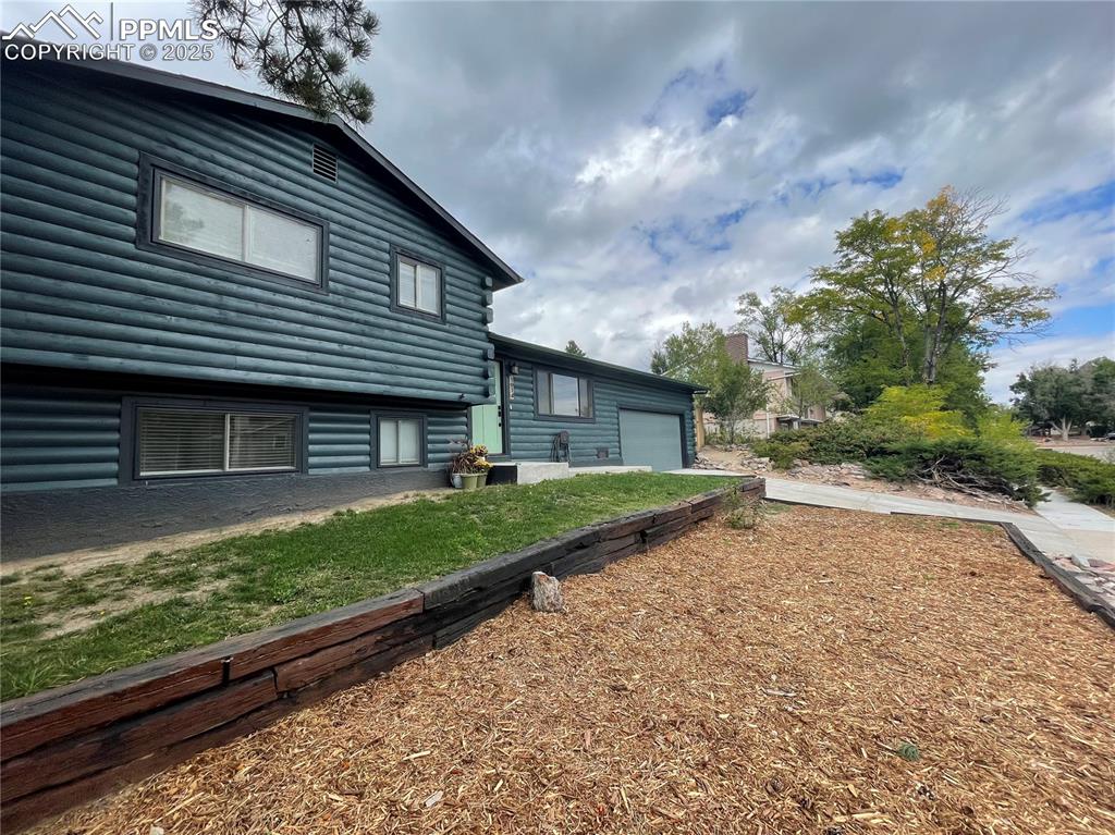 Image 6 of 39: Rear view of property with an attached garage, driveway, and faux log sidin