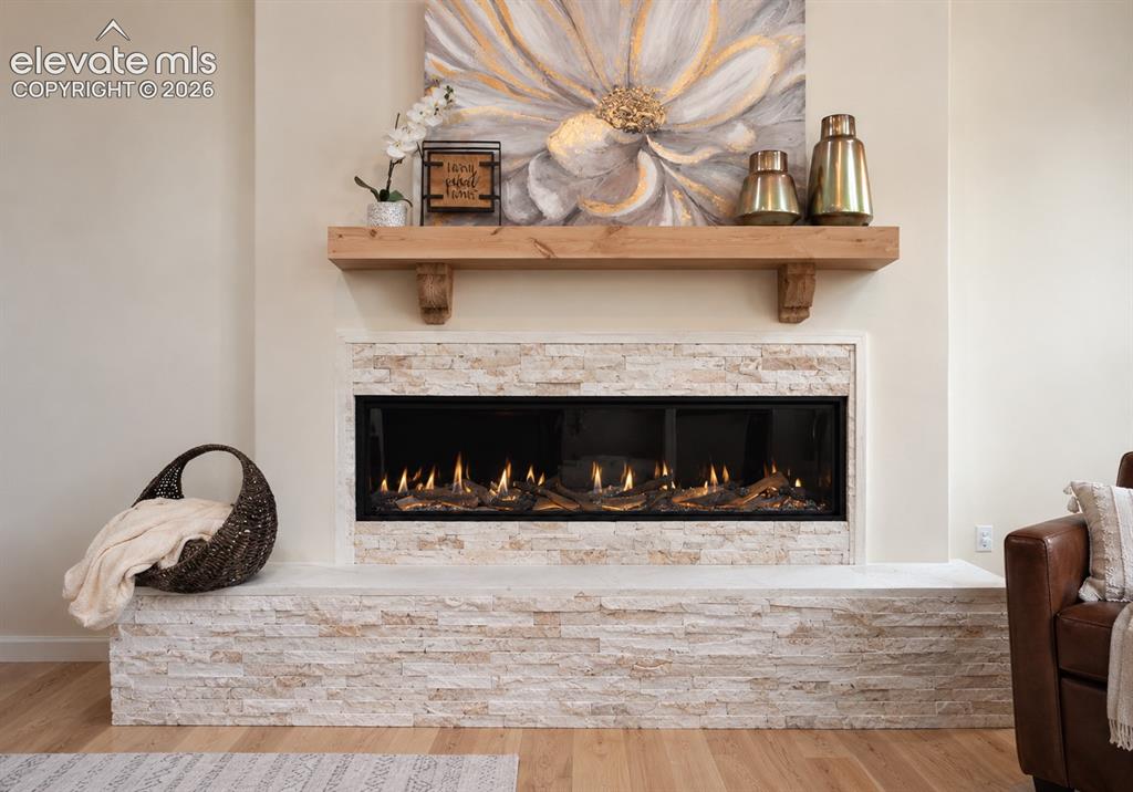 Image 21 of 49: Integrated linear fireplace with stone surround, wood mantel, and light woo