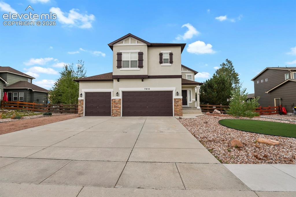 Caption: Two-story stucco exterior featuring stone accents, a two-car garage with panel doors, and a concrete