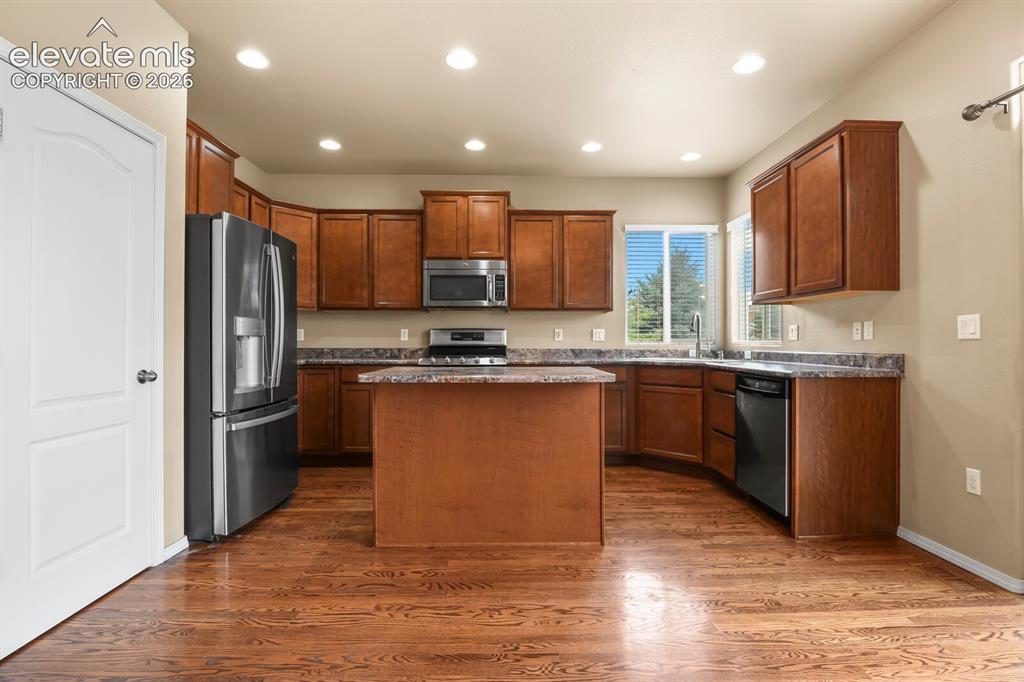 Image 15 of 50: Kitchen featuring wood-finish flooring, an island, wood cabinetry, stainles