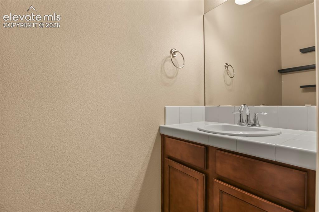 Image 20 of 50: Wood-finish vanity with a drop-in sink, chrome faucet, and white tiled coun