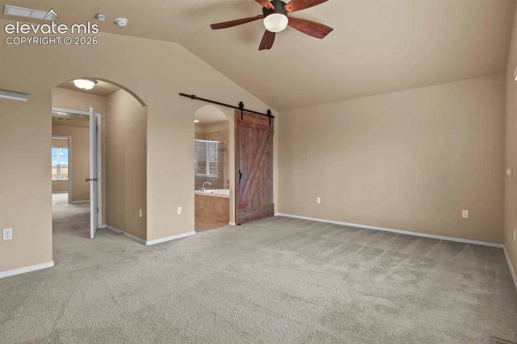 Image 24 of 50: Vaulted ceiling, ceiling fan, plush carpeting, arched doorways, and a slidi