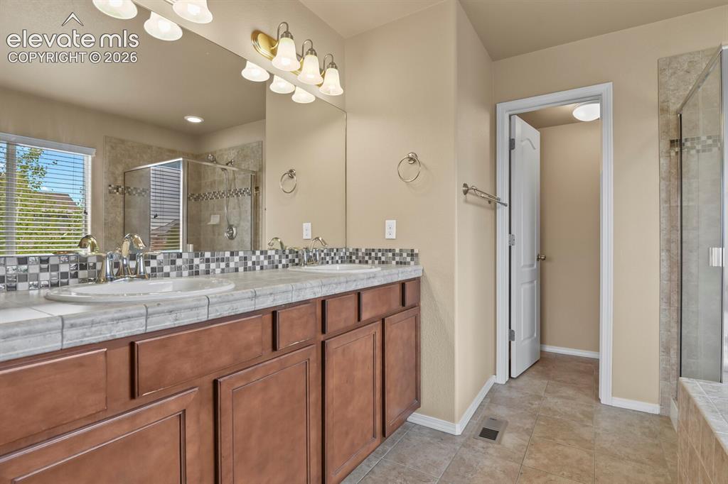 Image 26 of 50: Dual vanity with wood-finish cabinetry, tile countertop, and mosaic tile ba