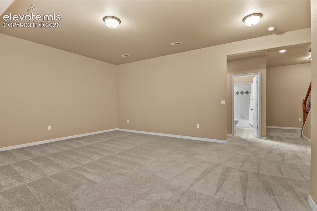 Image 37 of 50: Spacious room with neutral wall tones and patterned carpeting, featuring re