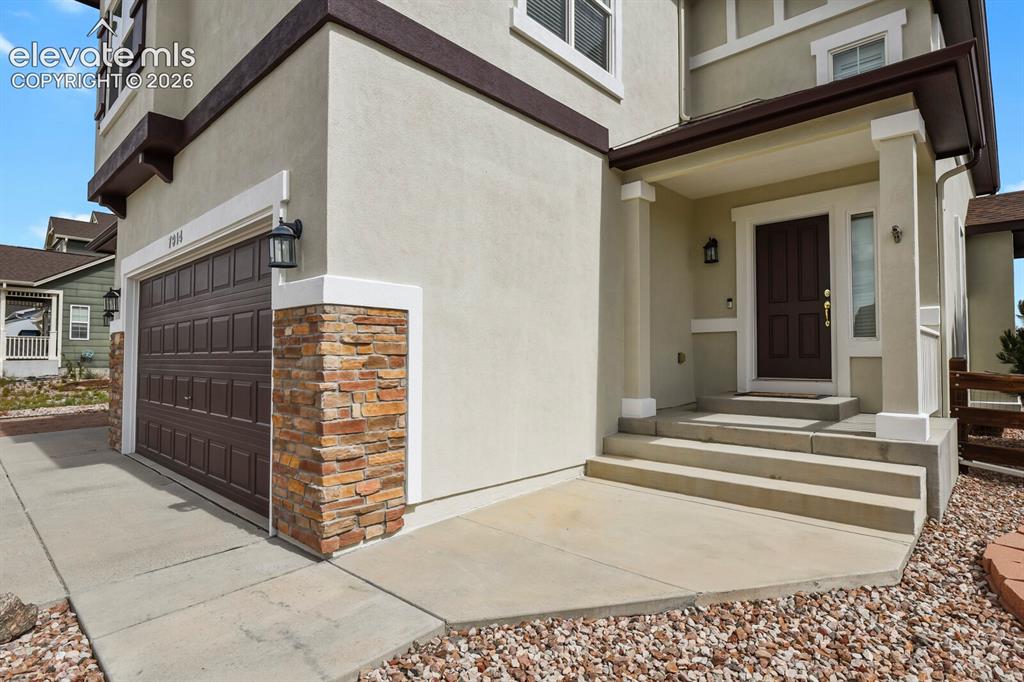 Image 5 of 50: Stucco exterior with stone veneer accents, covered entry porch, dark-panele