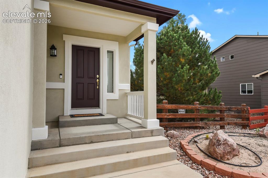 Image 6 of 50: Stucco exterior with a covered porch featuring square columns, a dark panel