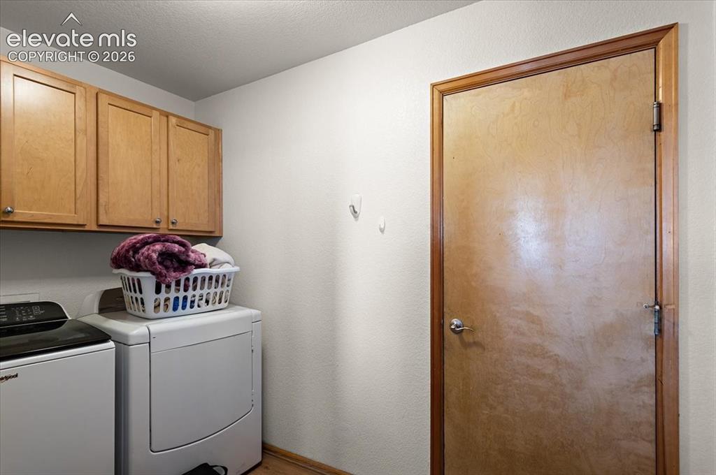 Image 16 of 47: Laundry area featuring upper wood-finish cabinetry with silver hardware, a