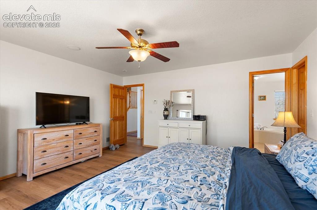 Image 20 of 47: Bedroom with wood-finish flooring, white walls, and a ceiling fan with inte