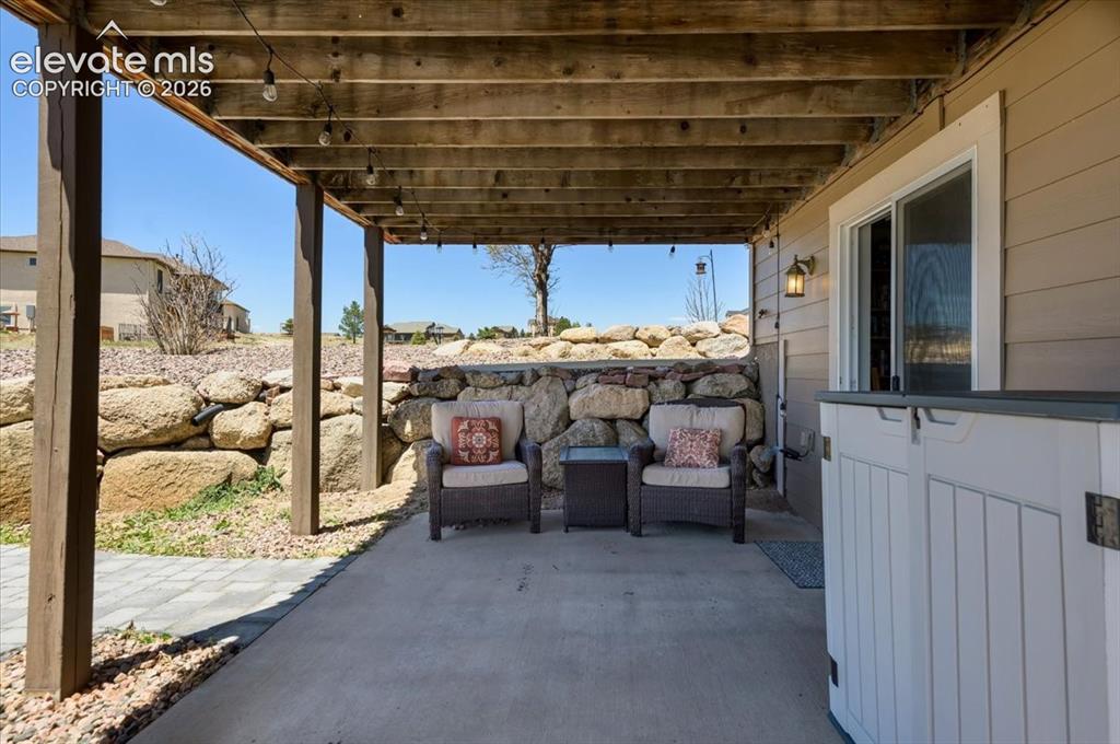 Image 41 of 50: Covered patio featuring a concrete slab floor, exposed wood ceiling beams, 