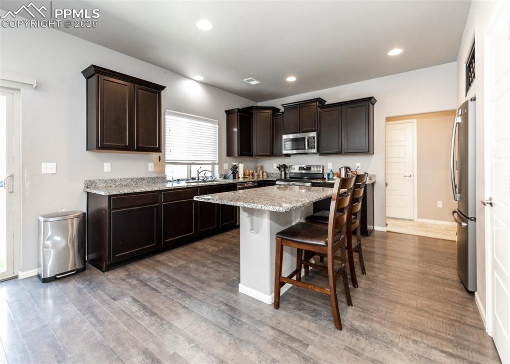 Image 11 of 40: Kitchen featuring dark brown cabinets, a kitchen bar, a kitchen island, app