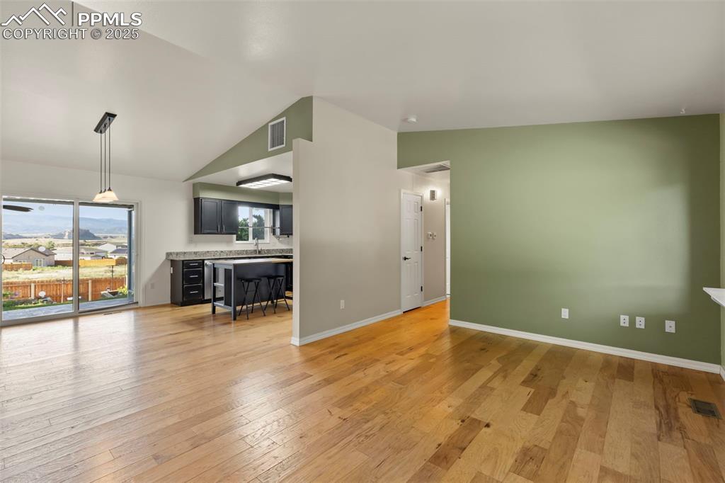 Image 4 of 27: Unfurnished living room with lofted ceiling and light wood-type flooring