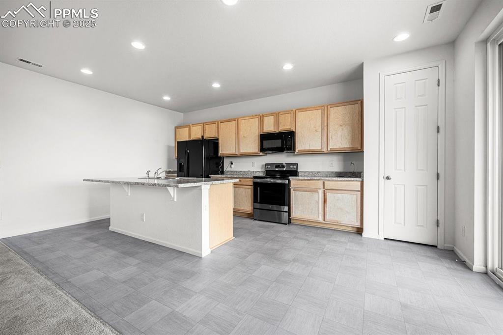 Image 11 of 25: Kitchen with black appliances, light brown cabinetry, a kitchen island with