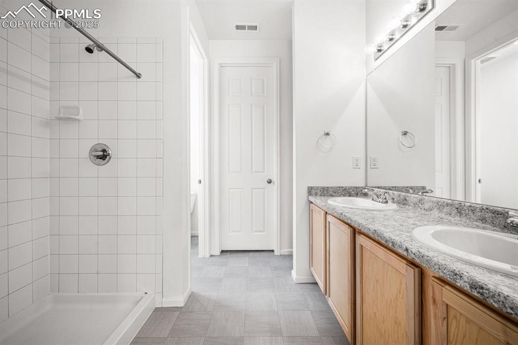 Image 14 of 25: Full bath featuring double vanity, tiled shower, and tile patterned floors