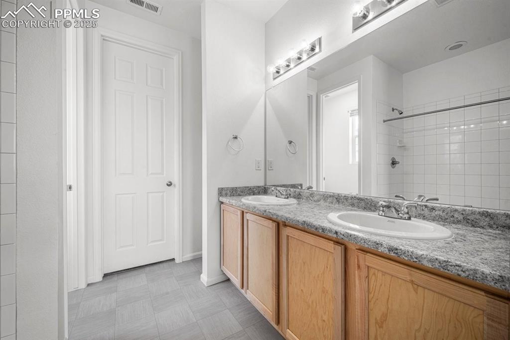 Image 15 of 25: Bathroom with double vanity, tiled shower, and tile patterned floors