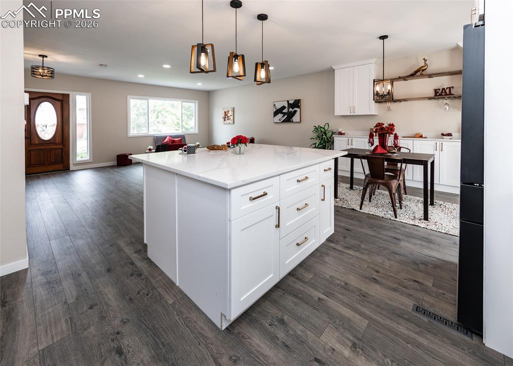 Image 10 of 48: Kitchen with white cabinetry, pendant lighting, a center island, open floor