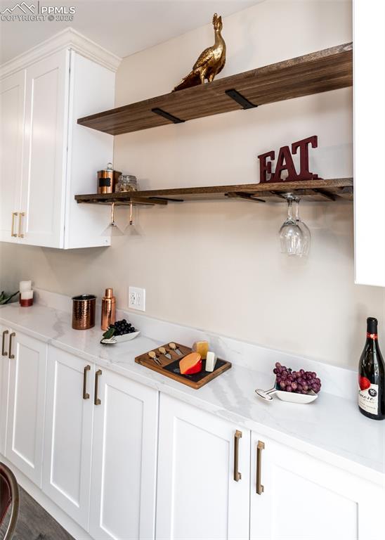 Image 17 of 48: Bar with white cabinets, open shelves, and light stone countertops